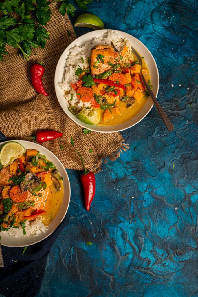 Flatlay shot of curry veggies over salmon filets and rice in bowls