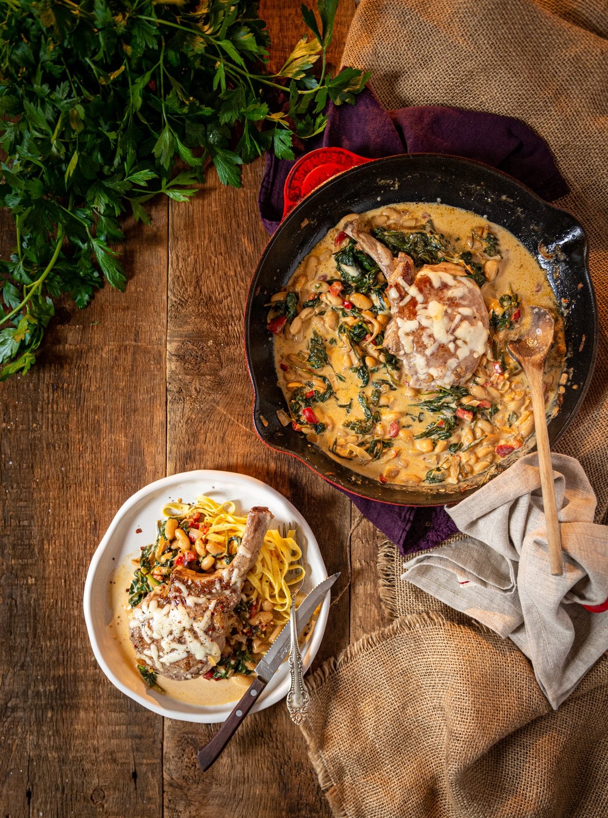 Overhead shot of cast iron skillet with creamy tuscan pork chops spinach and beans on a wooden table. 