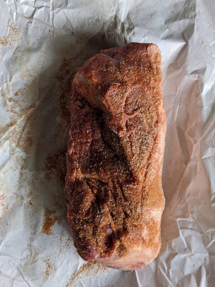 a pork shoulder rubbed with spices ready to be placed in the smoker.