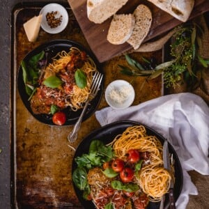 Beef parmesan with pasta on platters with greens and rustic bread