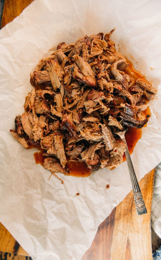 shredded smoked pork on parchment paper doused in vinegar sauce with a fork