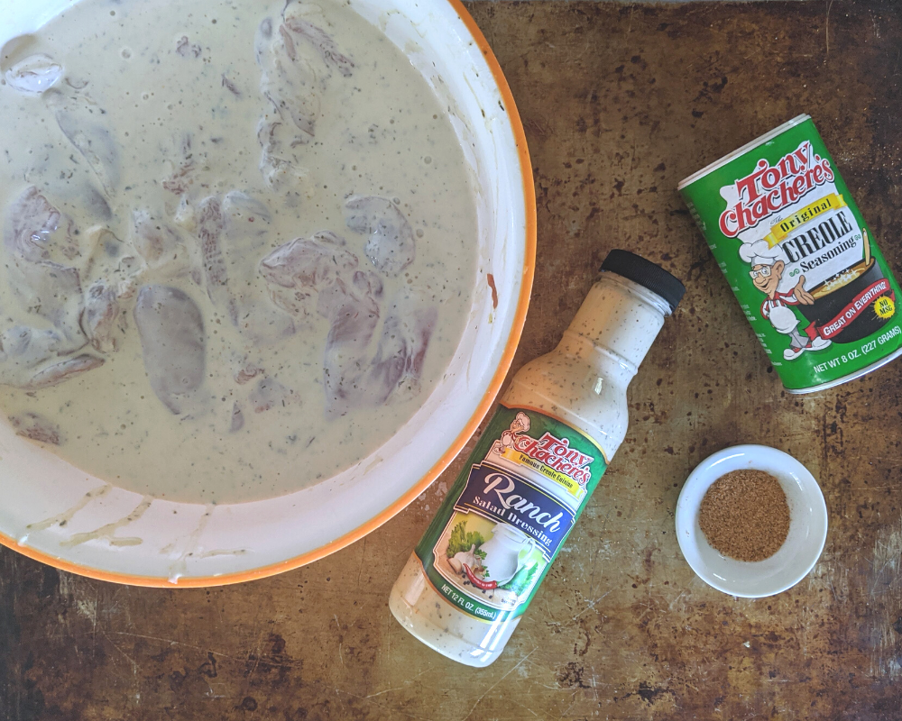 Chicken thighs marinating in creole seasoning and ranch dressing with buttermilk