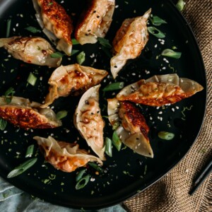 Salmon Potstickers on a black plate with sliced scallions and sesame seeds garnish