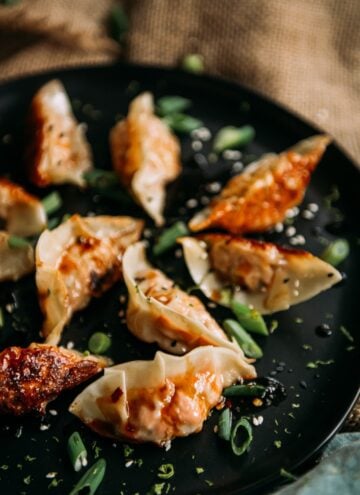 Homemade salmon potstickers on a black platter with crispy bottoms and scallions and sauce