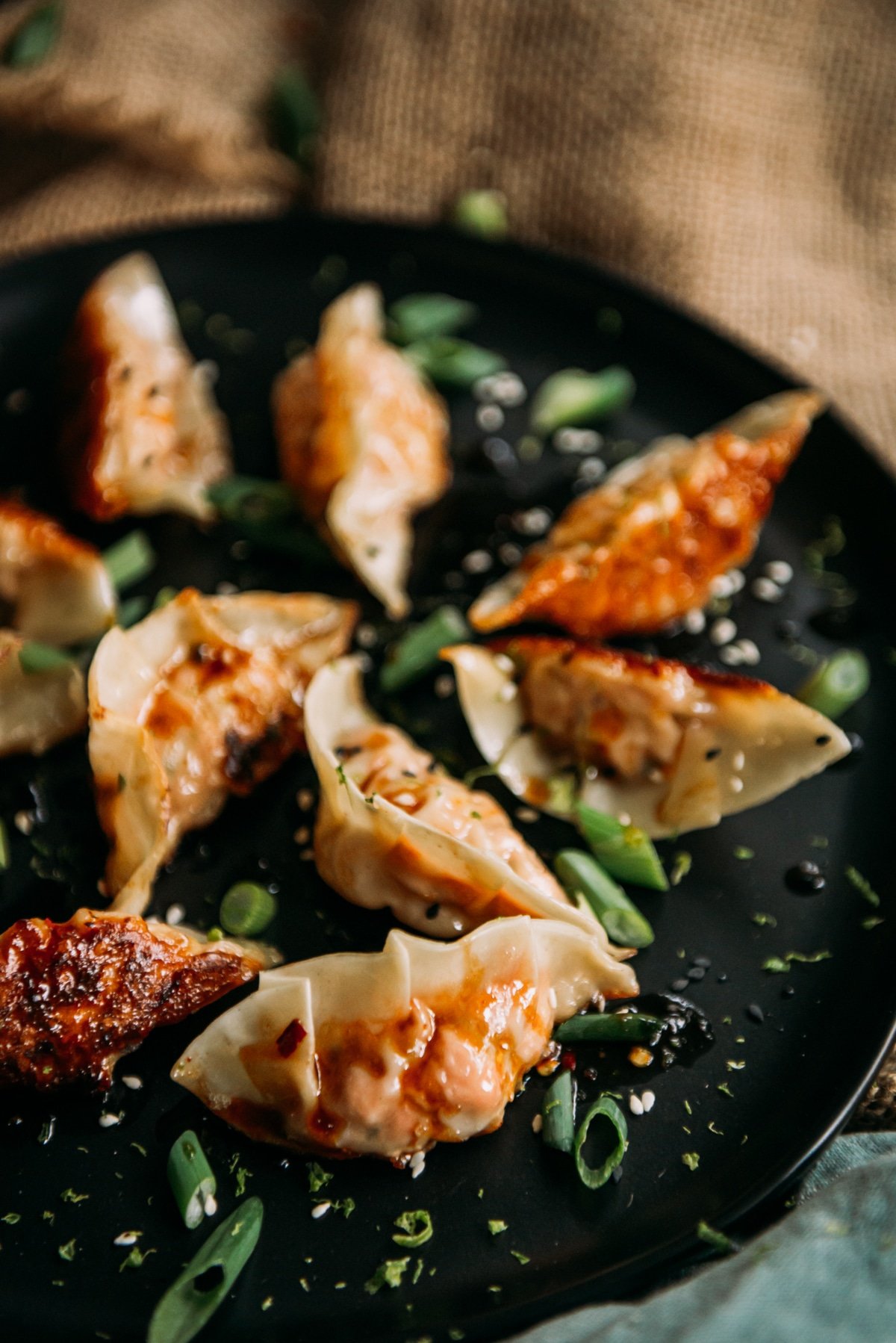 Homemade salmon potstickers on a black platter with crispy bottoms and scallions and sauce