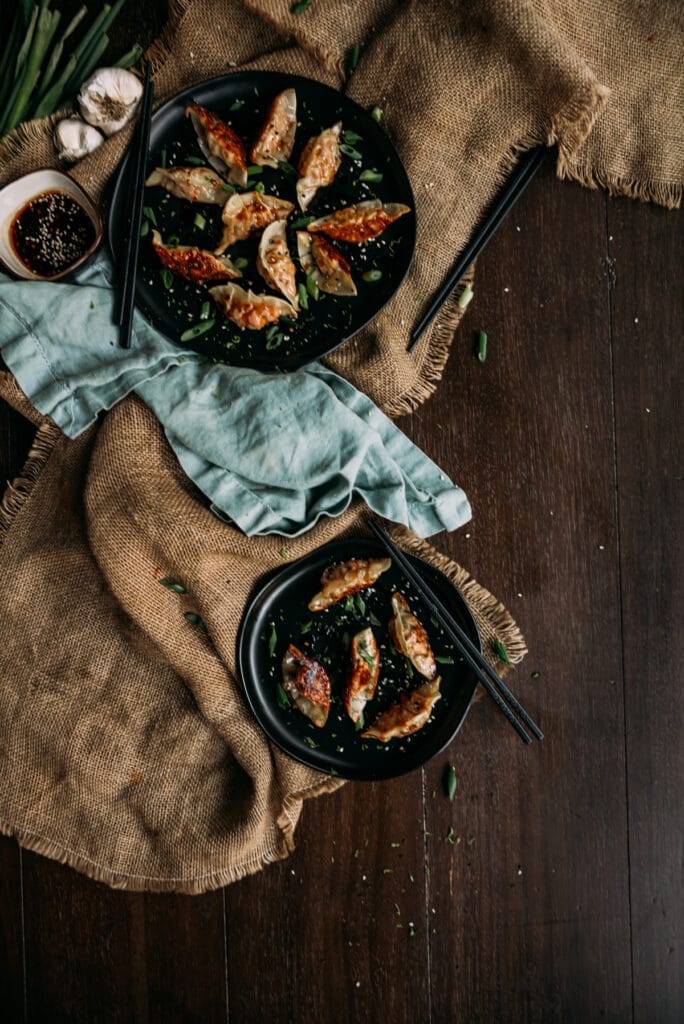 Flat lay image of cooked salmon potstickers with crispy golden brown bottoms, green scallion slivers and dipping sauce