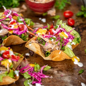 brightly colored and fresh - 3 fried tostada bowls filled with shredded carnitas, veggies, mangoes, pickled cabbage and crema