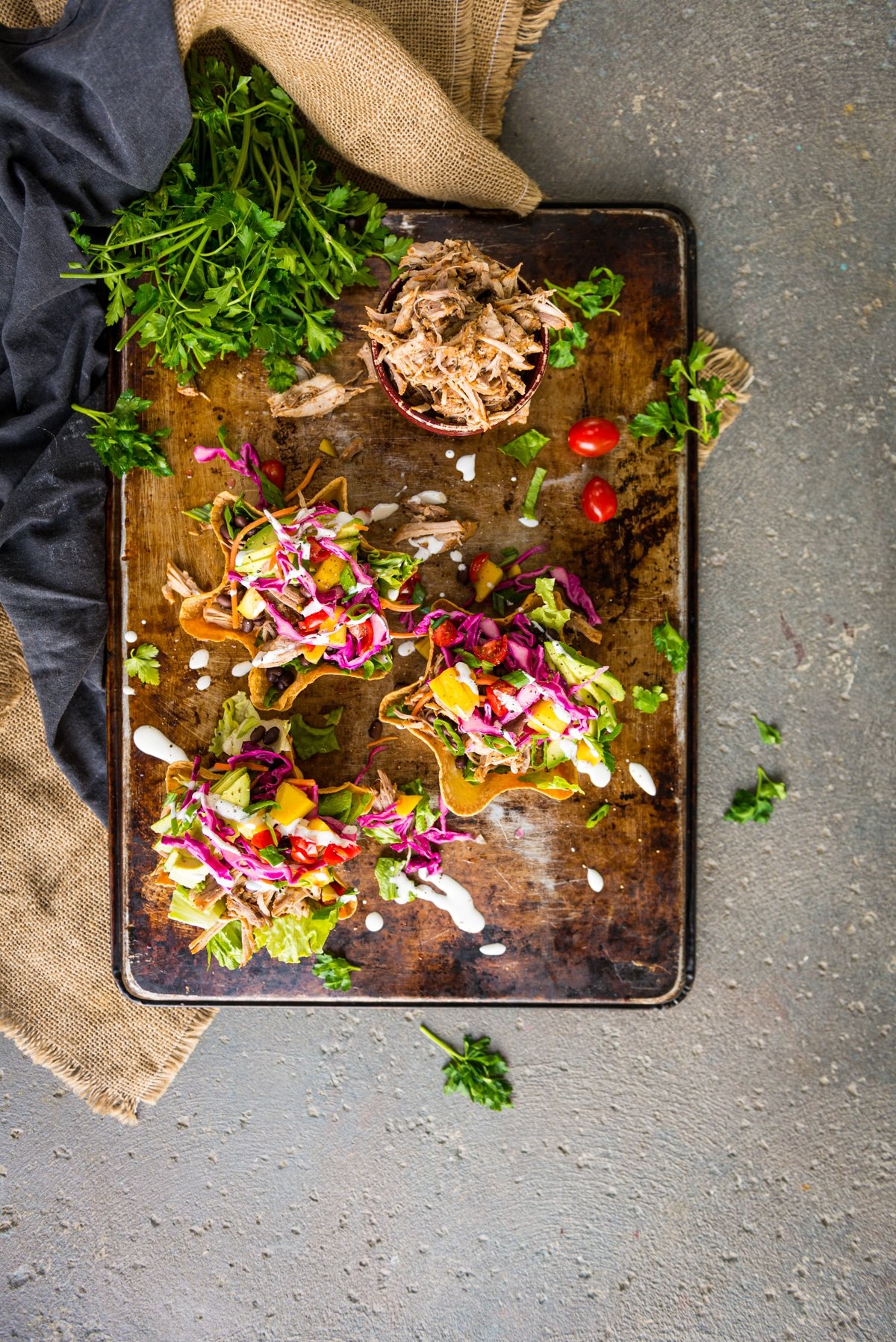 Flat lay view of 3 colorful fully loaded carnitas bowls topped with bright pickled cabbage, mangoes, avocado and crema 