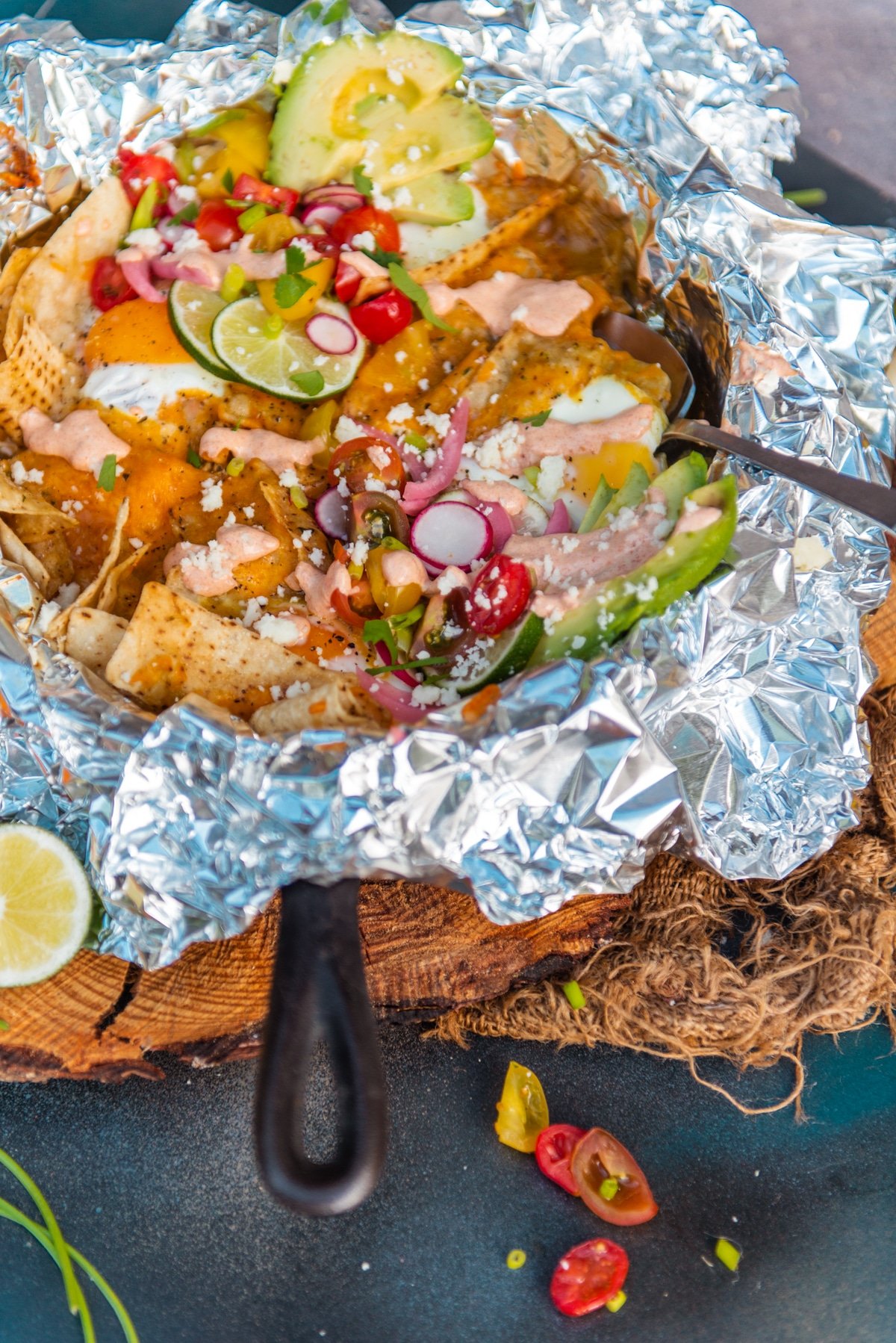 Close up of a grilled skillet of chilaquiles with leftover chicken, eggs and salsa verde topped with bright limes, radishes, tomatoes, and pickled onion