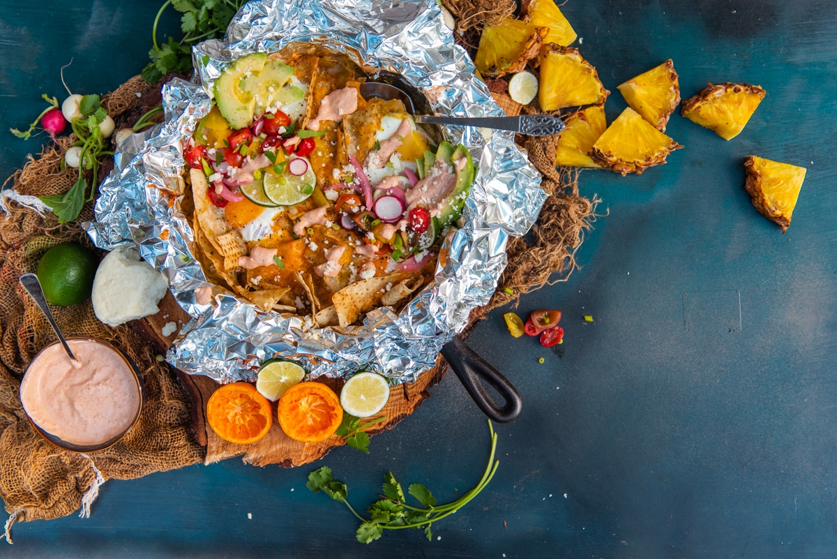 big skillet using leftover chicken with fried eggs on top, a quick crema and fresh toppings like sliced lime and grilled pineapple all in a foil skillet (shown in the cast iron pan as well for easy grilling)