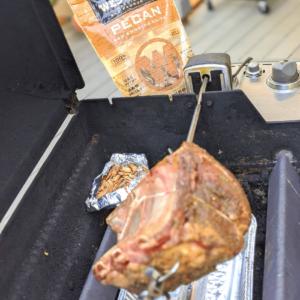 Standing rib roast on rotisserie with pecan wood foil packet on gas grill
