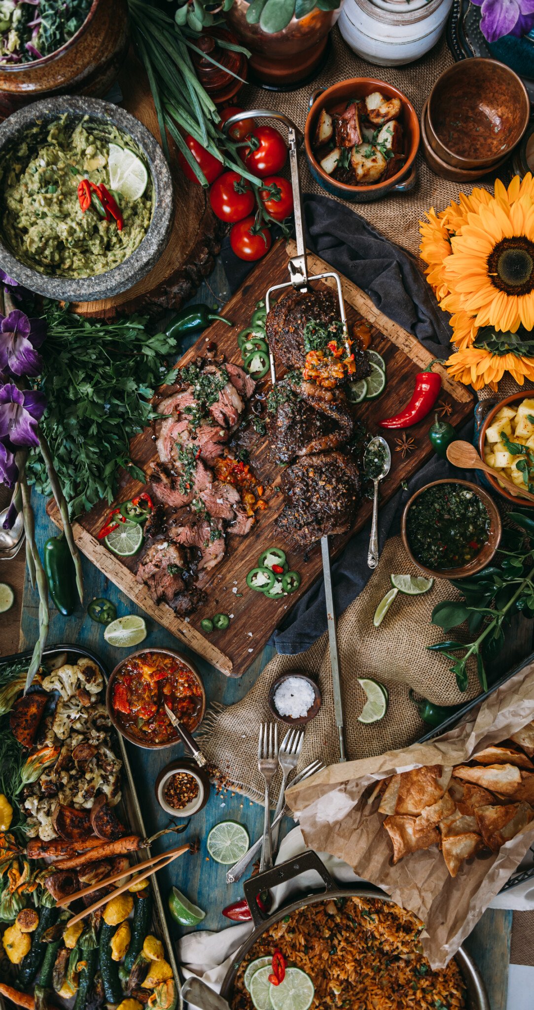huge spread of food centered around a rotisserie beef picanha with side dishes, flowers and various sauces