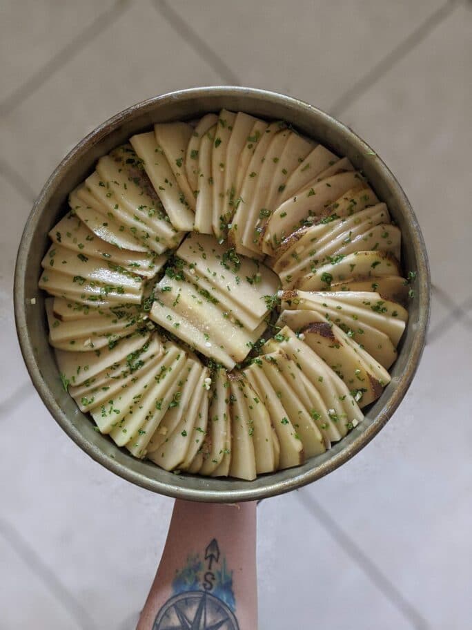 hand holding raw potatoes thinly sliced and layered in a pan ready to be baked