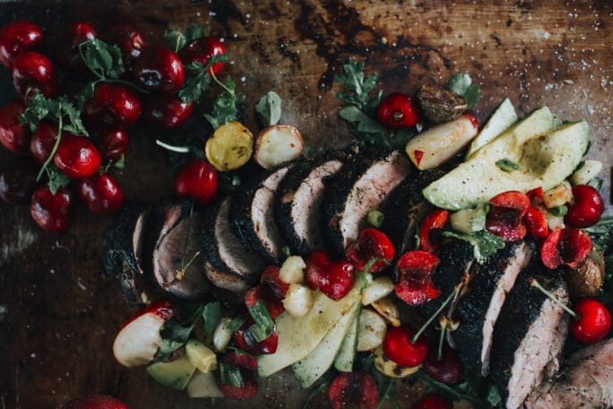 sliced pork tenderloin with bright red cherries and avocado slices 