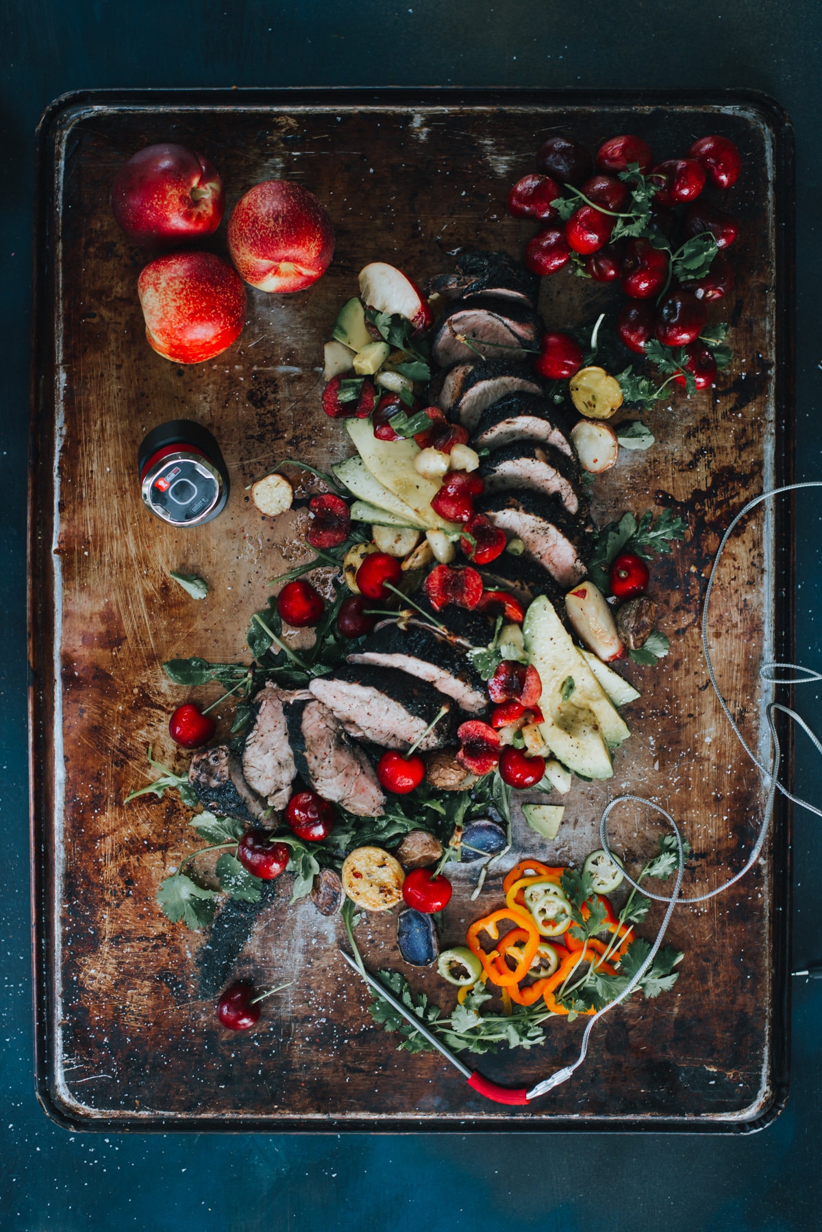 Above shot of a sliced grilled pork tenderloin topped with a fresh cherry and nectarine salsa with avocados and other various garnish