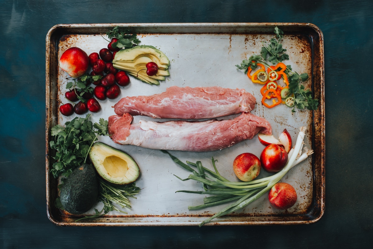 raw pork tenderloin on a sheet with ingredients around it for the recipe