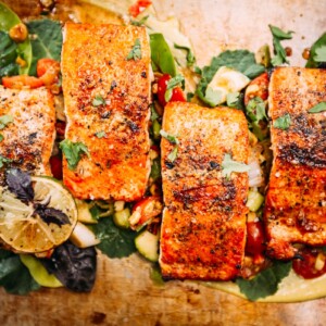 Grilled Sockeye Salmon filets plated over greens, summer succotash and cardamom aioli close up