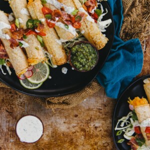 homemade air fryer potato stuffed taquitoes piled onto plated with a variety of toppings