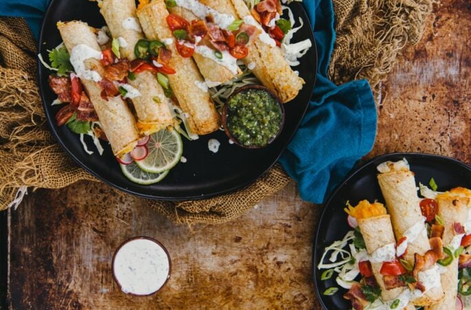 homemade air fryer potato stuffed taquitoes piled onto plated with a variety of toppings