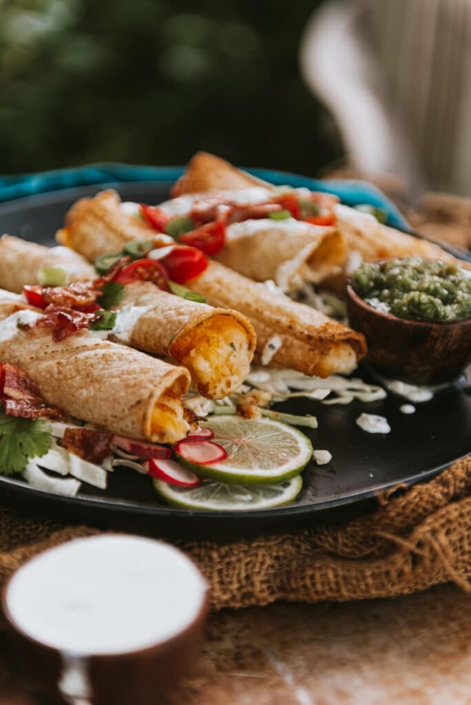 Plate with several air fried potato stuffed taquitos, a cream in the foreground and topped with quick pico