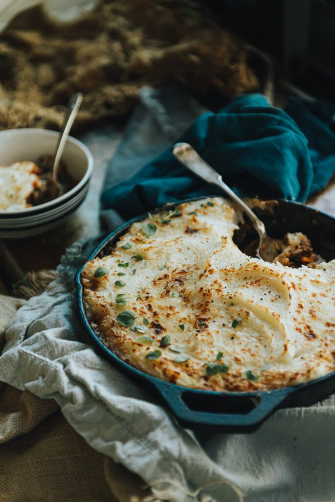 Creamy mashed potato topped shepherd's pie with Moroccan spices and a heaping portion taken out in a bowl on blue cloths 