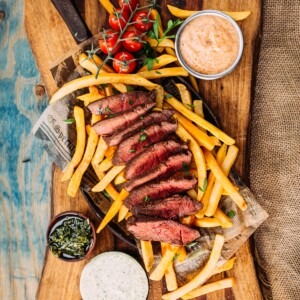 Above shot of flat iron, sliced to show pink center, fries and a variety of dipping sauces on a wooden background