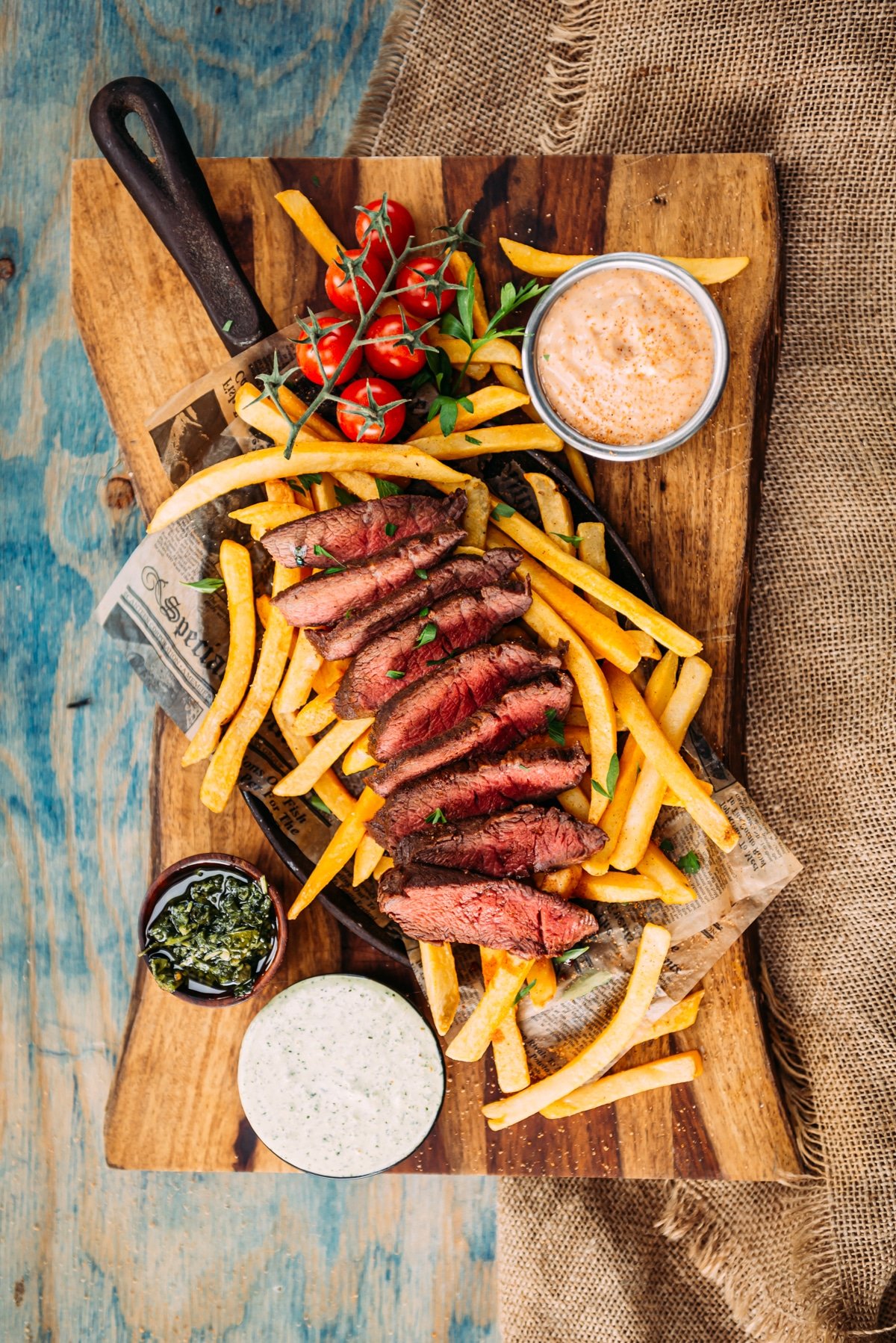 Above shot of flat iron, sliced to show pink center, fries and a variety of dipping sauces on a wooden background 