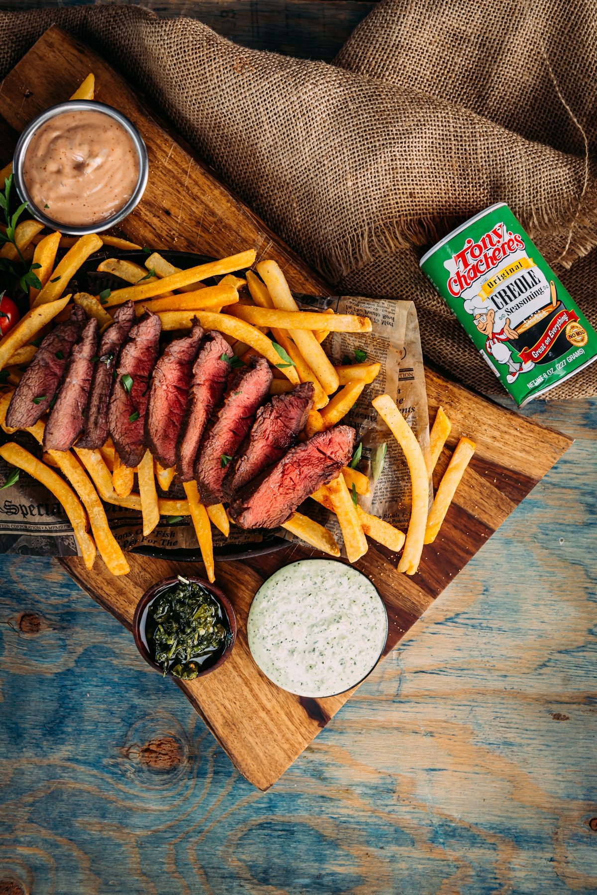 Over head shot of sliced flat iron steak with fries, dipping sauces on a wooden board.