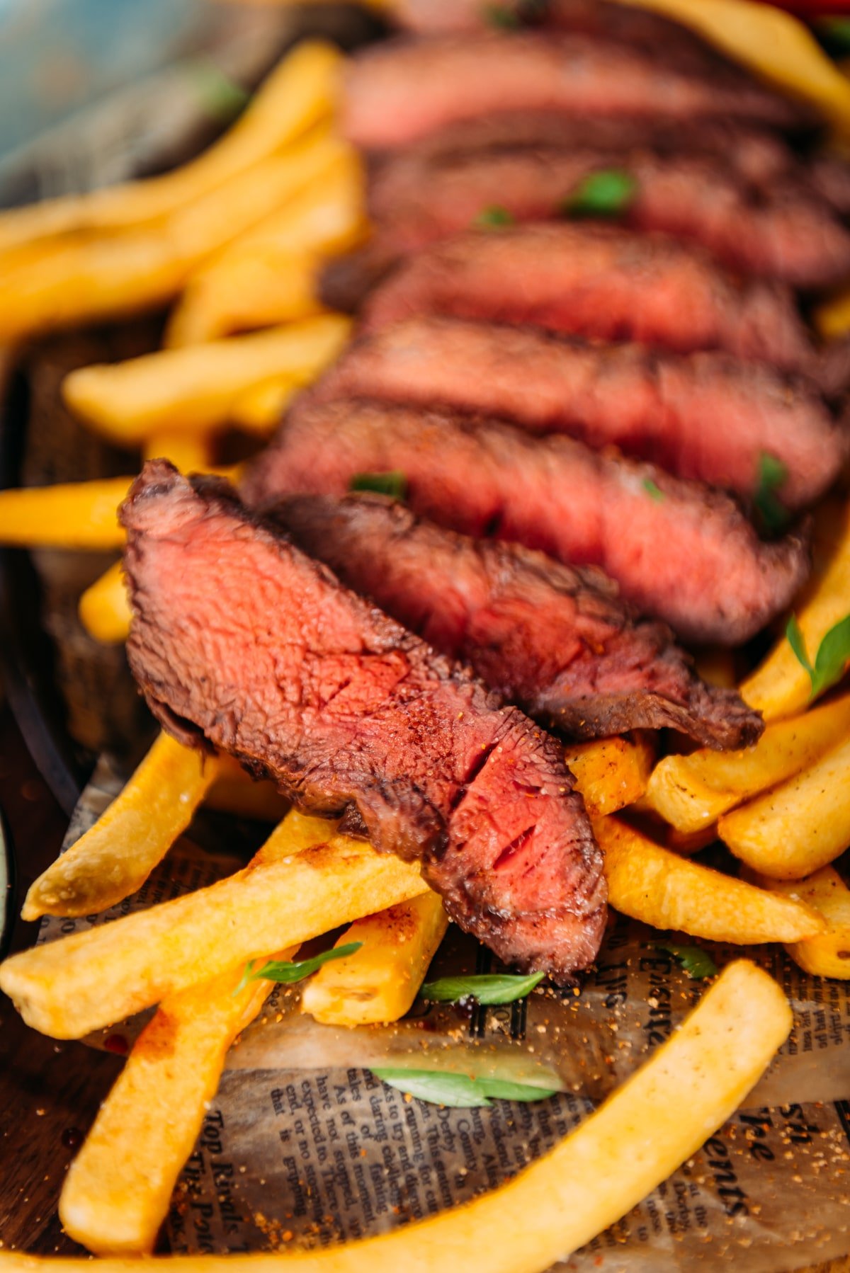 Close up of sliced flat iron - served medium rare after a sous vide cook for perfect pink slices over a bed of french fries.