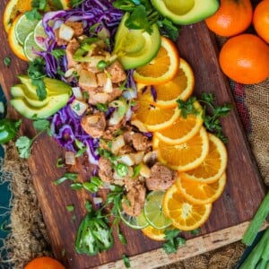 mojo pork bites over sliced citrus and chopped red cabbage on a cutting board