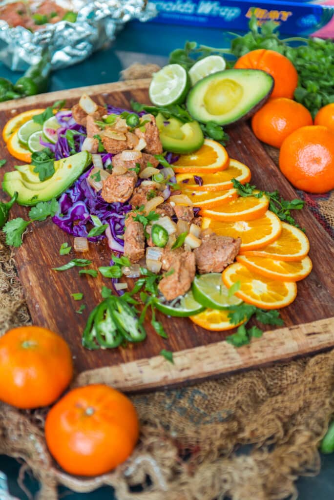 Cutting board loaded with tender pork bites spooned out over fruit and other veggies for serving 