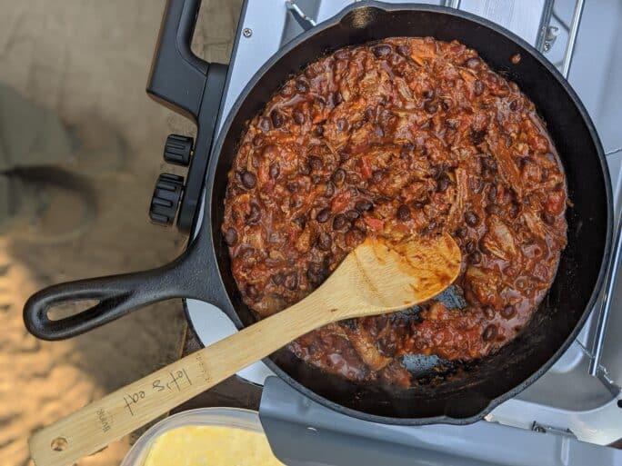 leftover pork chili being heated in cast iron on a camp stove