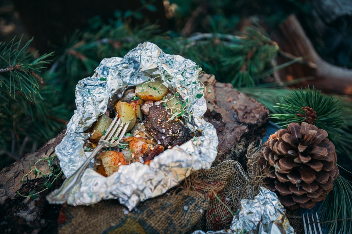 Opened foil wrapped steak and potatoes on log with fork