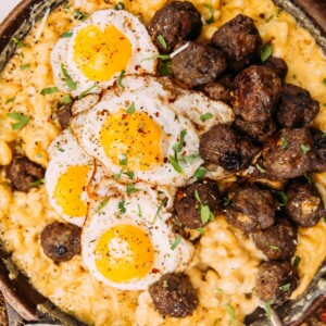 a skillet of macaroni and cheese with meatballs and fried eggs