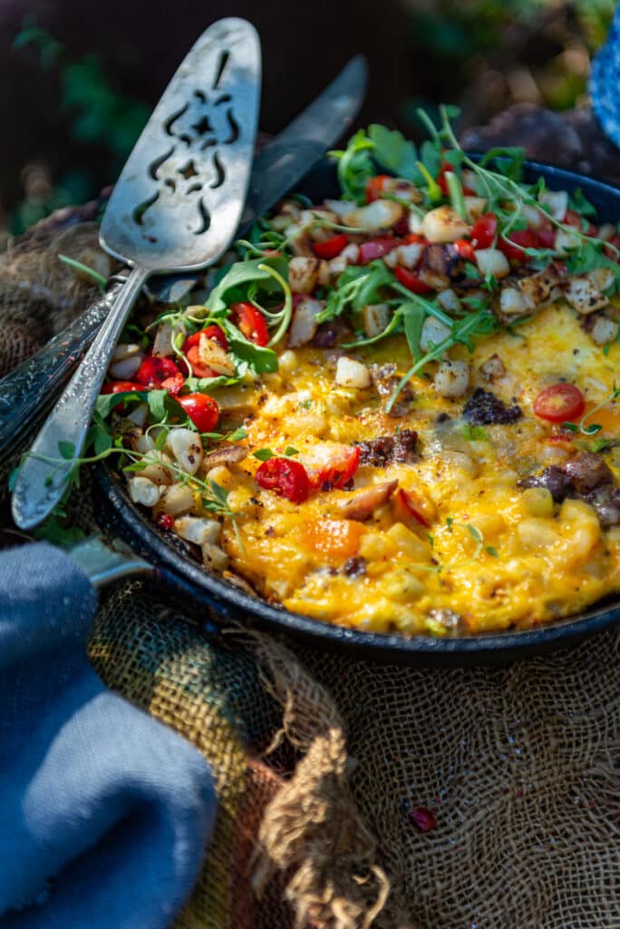 Skillet with beautiful egg frittata with colorful arugula, potatoes and toamtoes on top. 