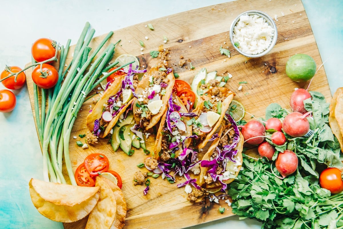 Overhead shot of pork tacos in fried tortillas on a cutting board with all the toppings. 