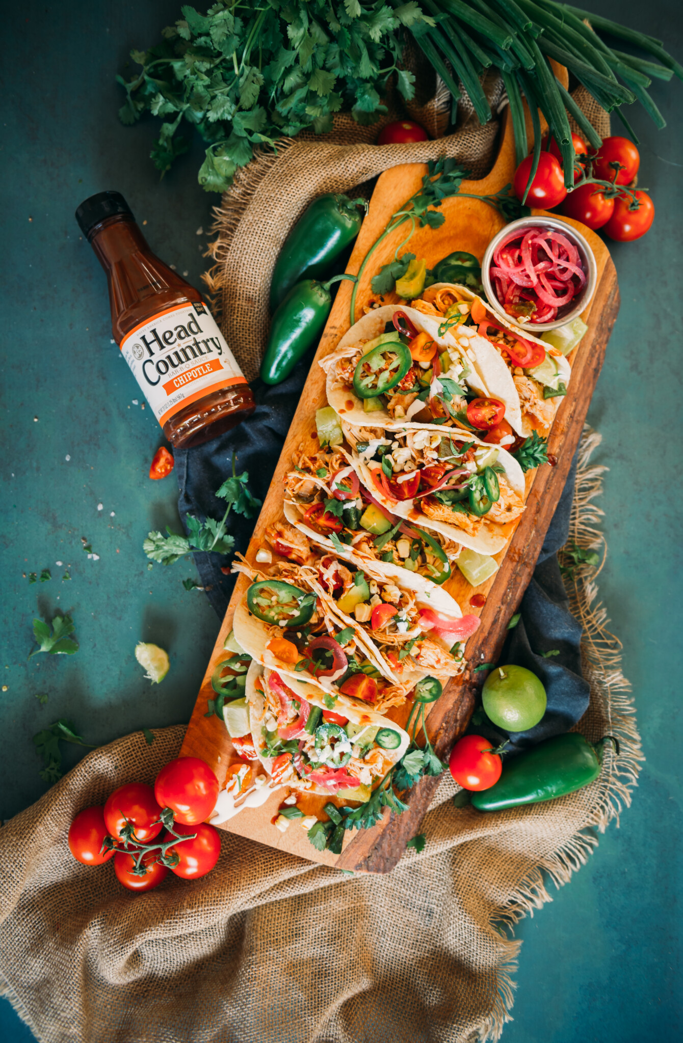 Chipotle Chicken Tacos served in a wooden tray with pickled onions and colorful garnish. 