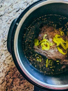 chuck roast in insta-pot with other ingredients ready to be cooked