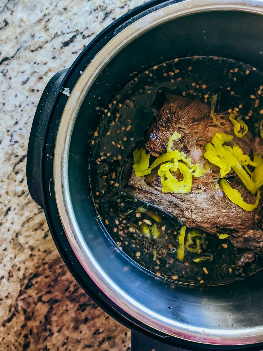 Chuck roast in insta-pot with other ingredients ready to be cooked.