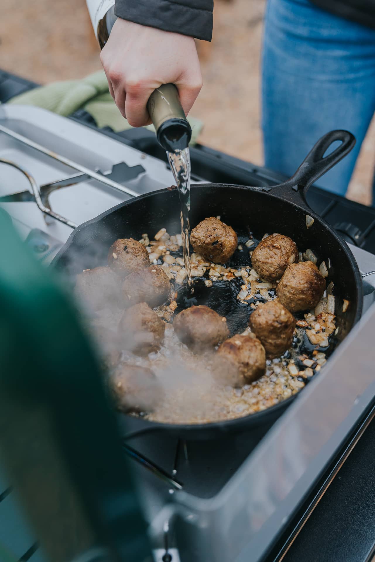 White wine being added to cast iron pan with meatballs.