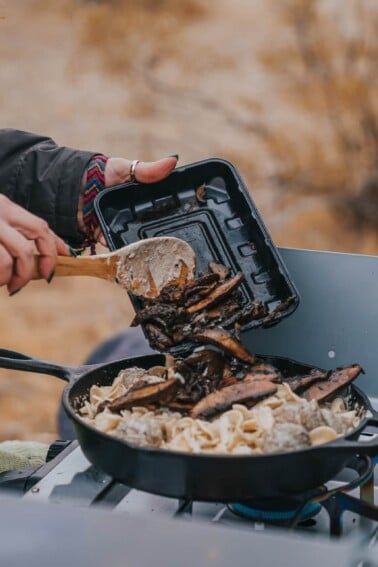 Adding mushrooms to pan - outdoor cooking on camp stove