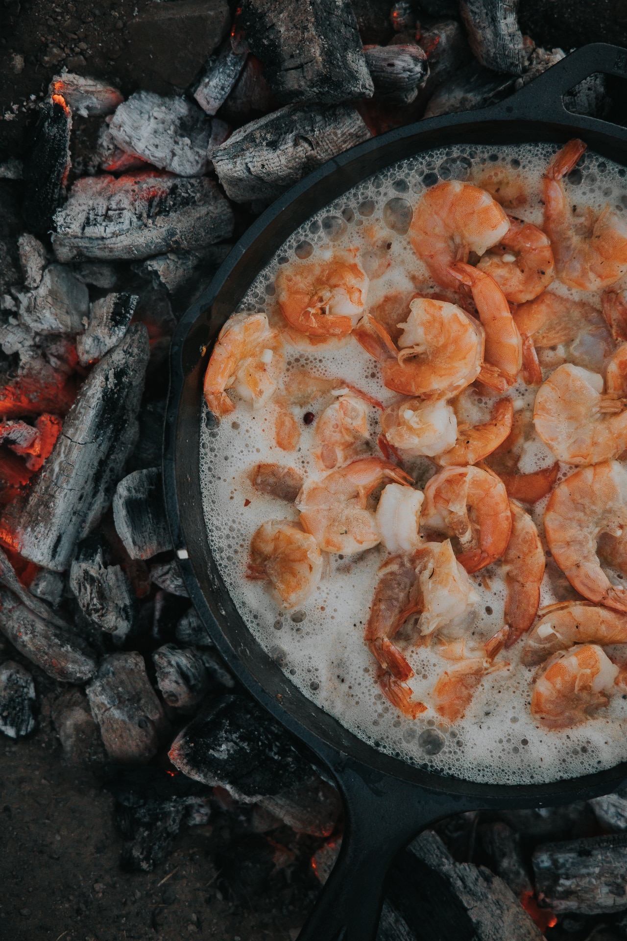 Cast iron pan on coals with shrimp cooking and butter bubbling 