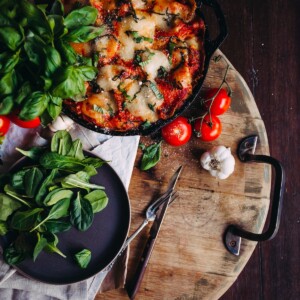 flat lay of the full skillet of lasagna with fresh ingredients to of garlic, basil and tomatoes