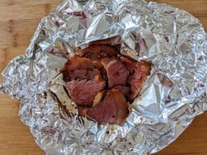 steamed pastrami in foil on cutting board ready to be served