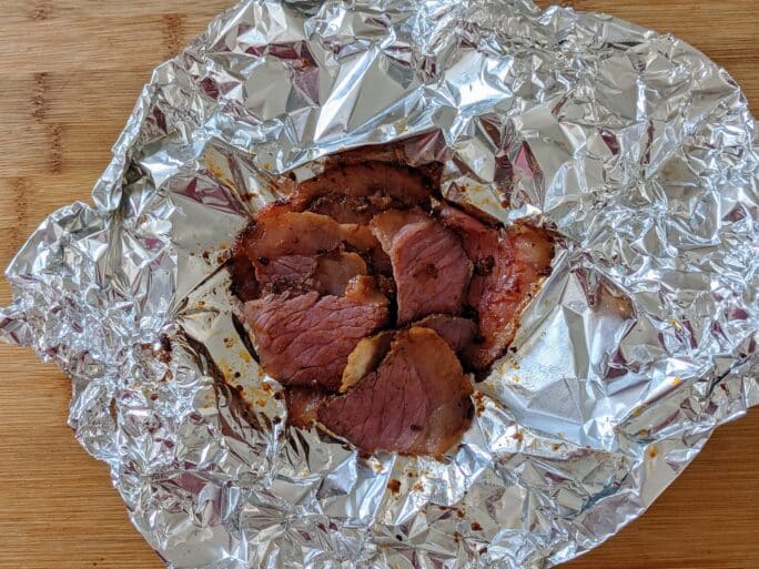 steamed pastrami in foil on cutting board ready to be served
