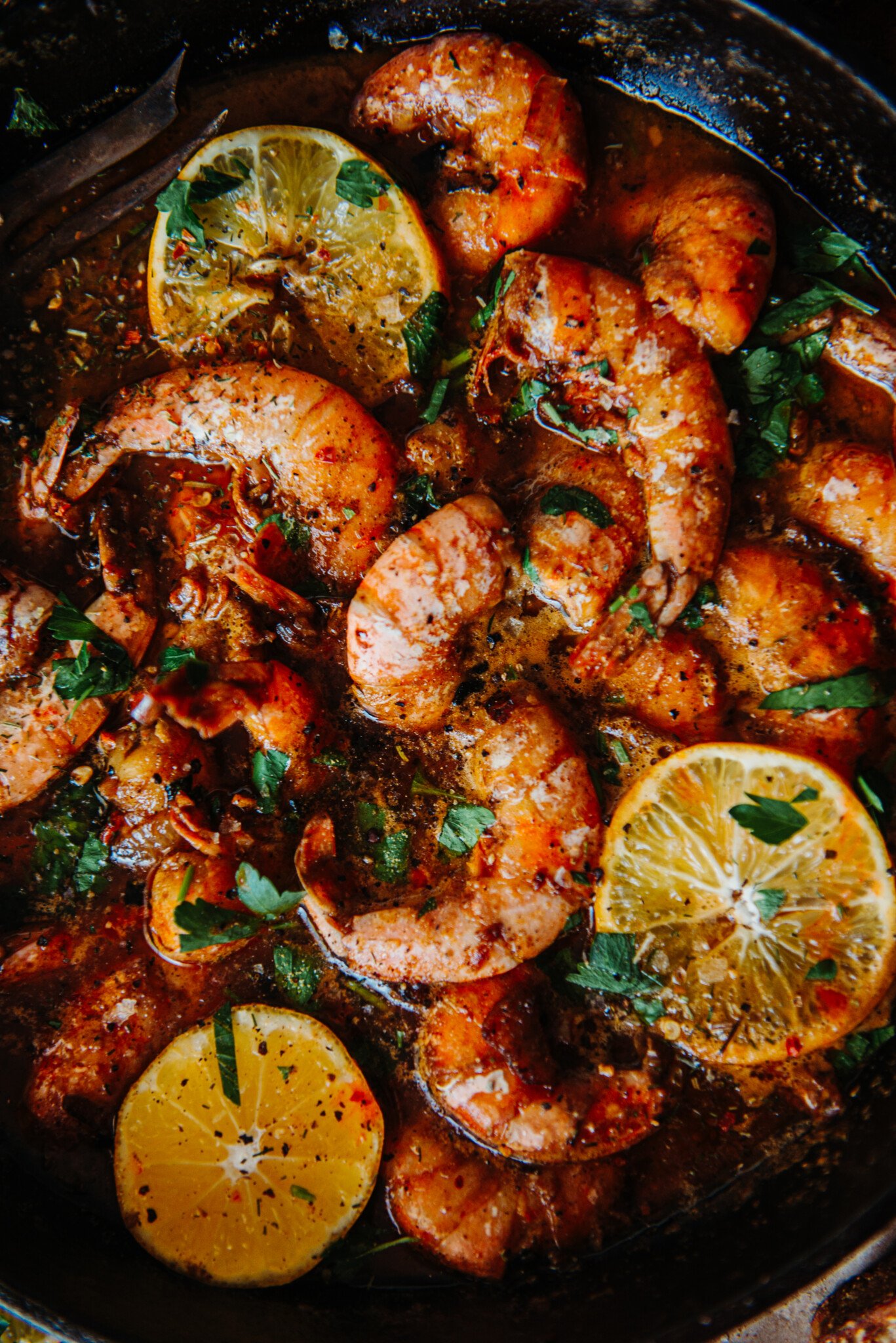 Cast Iron New Orleans BBQ Shrimp with bright slices of lemon and fresh parsley.