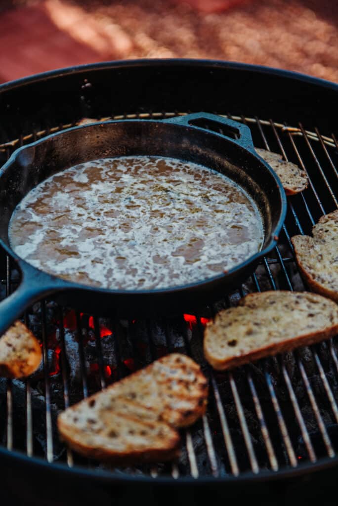 bubbling sauce in cast iron skillet with bread being toasted for New Orleans BBQ Shrimp