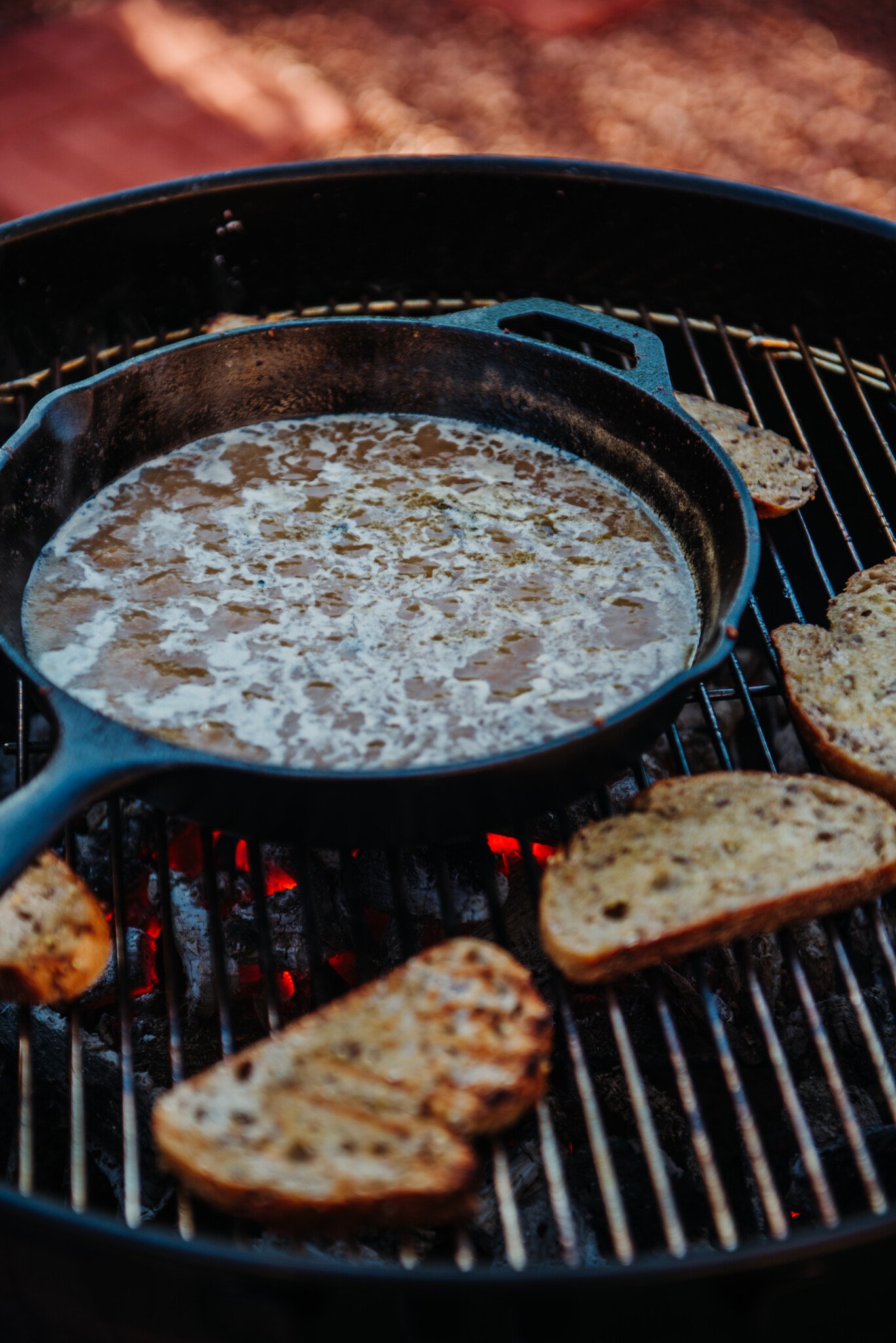 Bubbling sauce in cast iron skillet with bread being toasted for New Orleans BBQ Shrimp.
