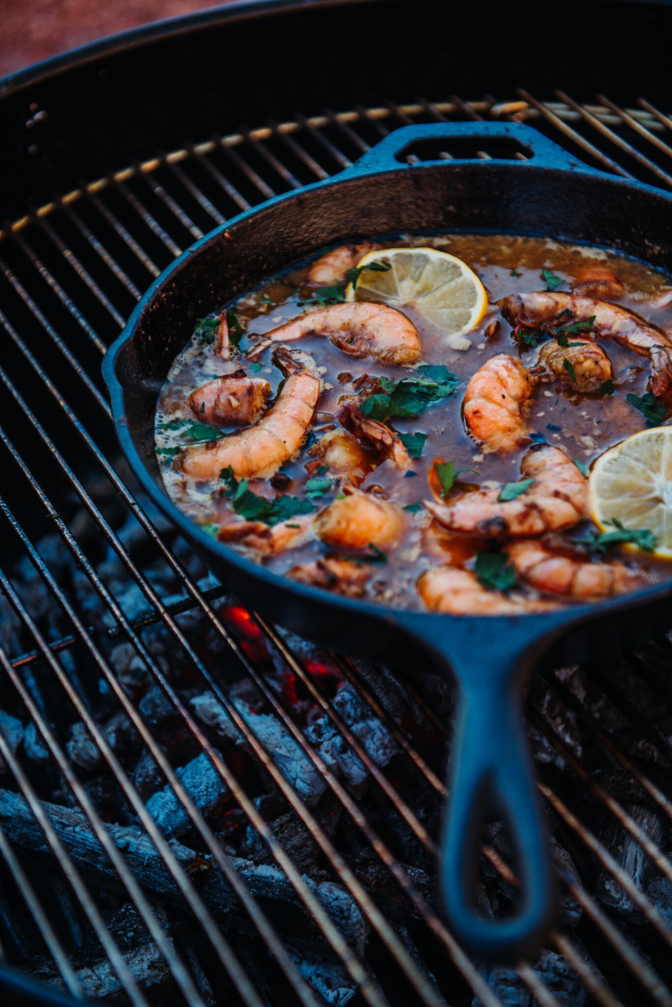 Showing coals and grilling New Orleans BBQ Shrimp in skillet.