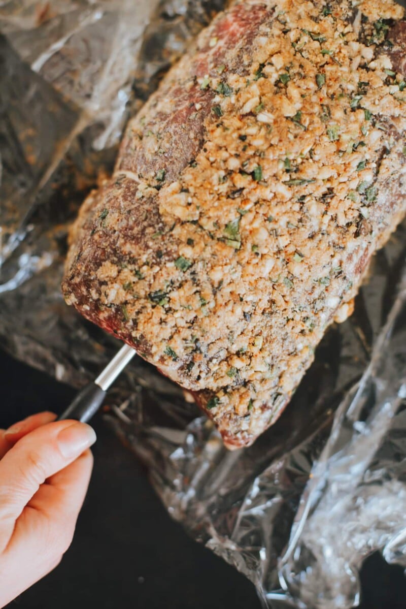 roast coated in garlic and herbs with thermometer being inserted
